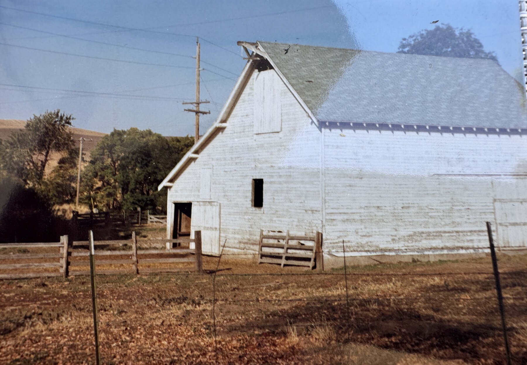 White barn with fence line and wheat hills beyond