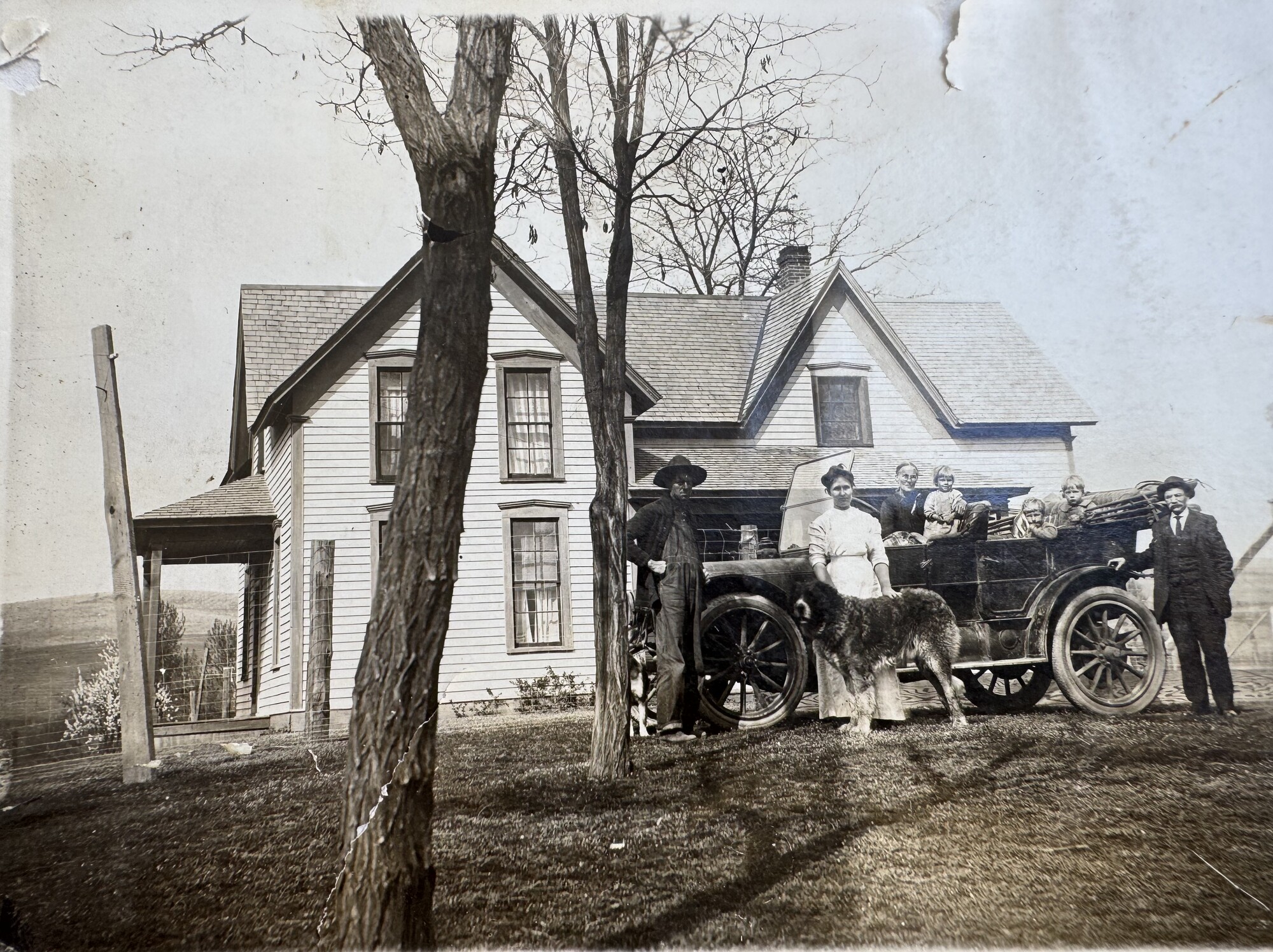 Farmhouse with family gathered around an early automobile